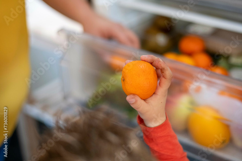 Mother giving her son a healthy snack, fruit from the fridge photo