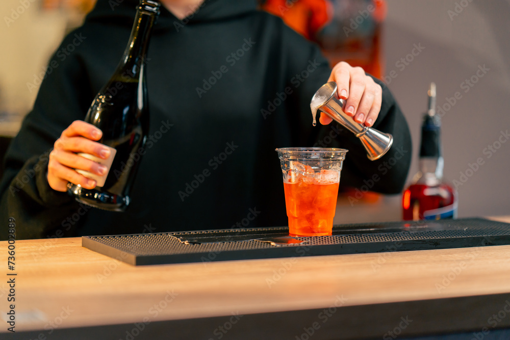 a young girl at the bar pours the required amount of alcohol with a measuring cup into a cocktail