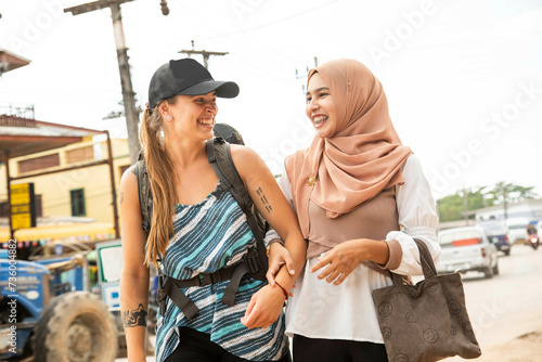 Two young women one wearing a Hijab walk together arm in arm smiling  in a rural town in Thailan photo