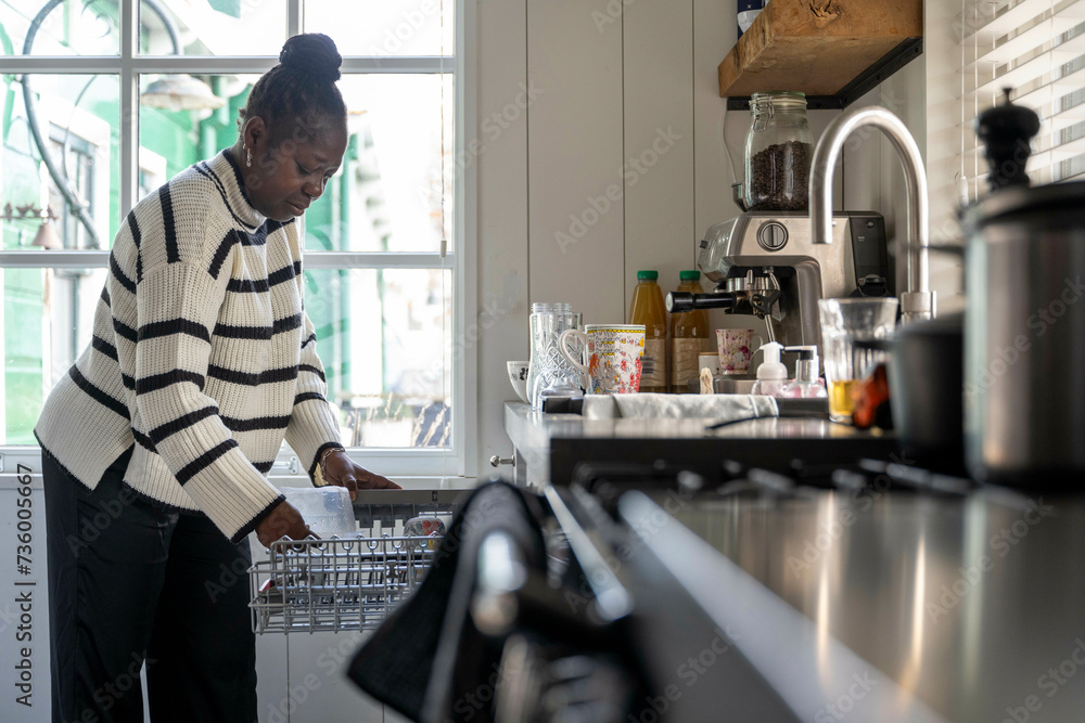 Female cleaning her kitchen loading the dishwasher Female cleaning her kitchen loading the dishwasher