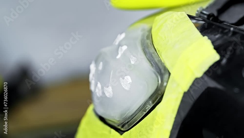 Caucasian man polishing headlights of a car using yellow polisher.