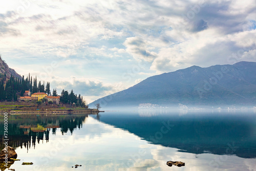 Bay of Kotor (Boka kotorska) on cloudy misty day. Calm water and sky reflected in water surface. Banja Monastery at background. Scenic nature background or wallpaper. Kotor, Montenegro