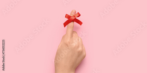 Female hand with red bow on index finger against pink background. Reminder concept