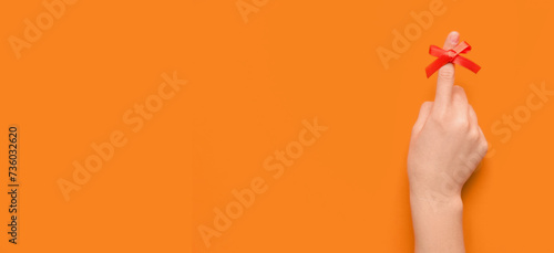 Female hand with red bow on index finger against orange background with space for text. Reminder concept photo