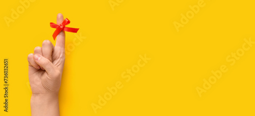 Female hand with red bow on index finger against yellow background with space for text. Reminder concept photo