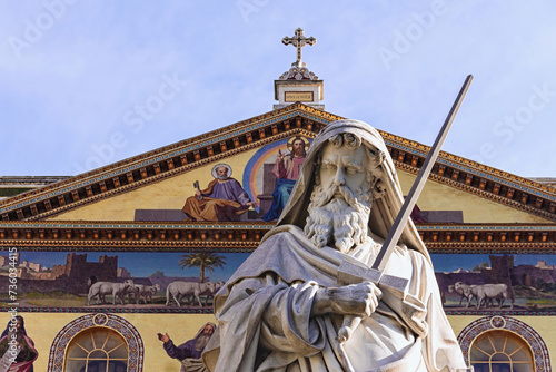Statue of Saint Paul. Fragment. Facade of Basilica of Saint Paul Outside the Walls (Basilica Papale di San Paolo fuori le Mura) at background. Rome, Italy
