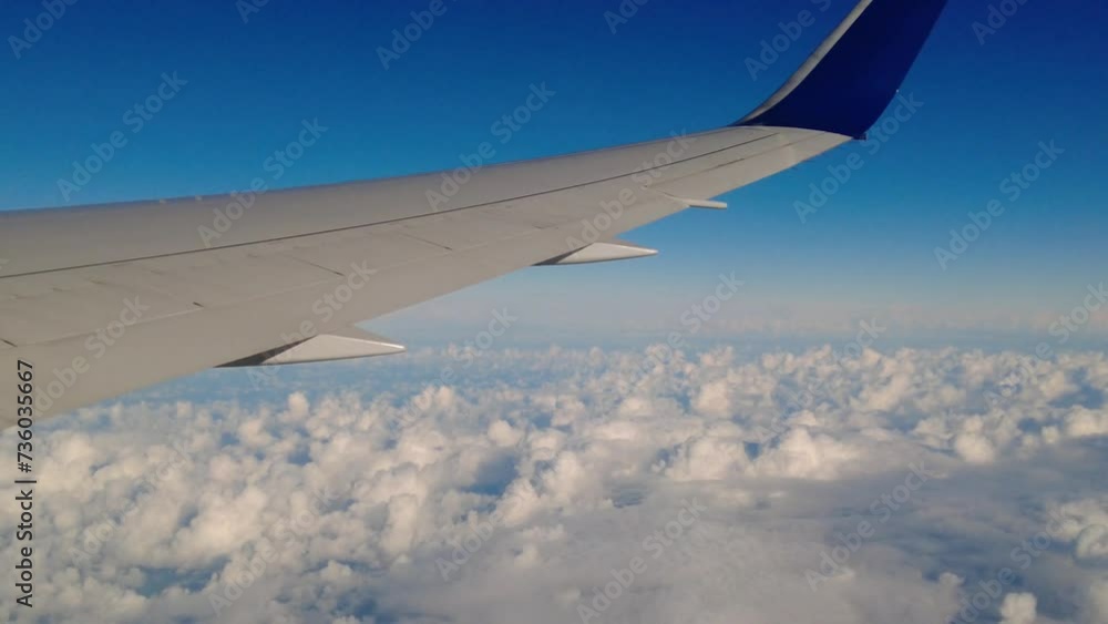 Panning shot of airplane wing while flying at high altitude blue skies clouds underneath Panning shot of airplane wing while flying at high altitude blue skies clouds underneath
