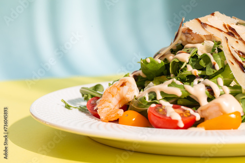 Fresh salad with greens, tomatoes, grilled shrimps on white plate. On yellow background.