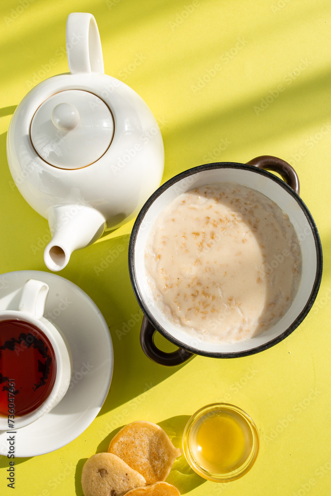 Warm and Inviting Breakfast Scene with Oatmeal, Tea, and Honey on Yellow Background Warm and Inviting Breakfast Scene with Oatmeal, Tea, and Honey on Yellow Background