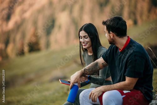 Couple in workout attire taking a breather after jogging, staying hydrated and monitoring fitness metrics on their devices photo
