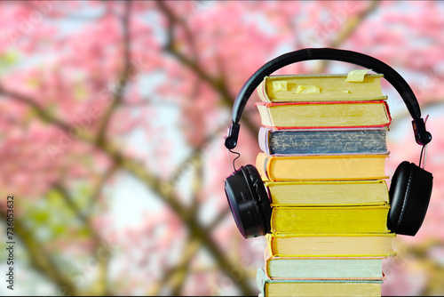 Relaxing with audiobooks during springtime season with heap of books and vintage headphones. Beautiful blooming cherry tree in the back, focus on the foreground