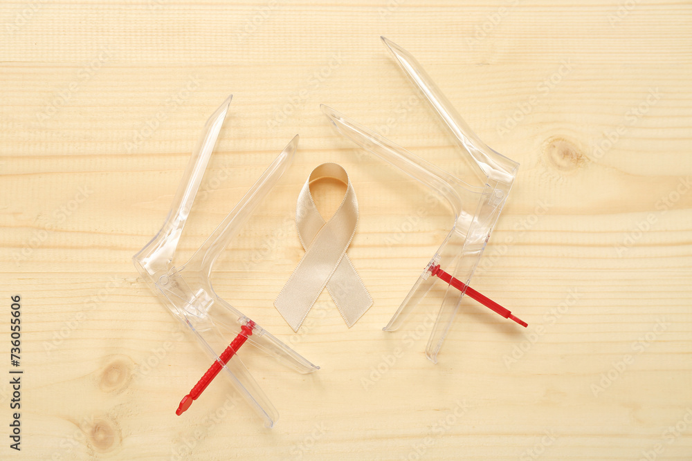 Beige ribbon with gynecological tools on light wooden background. Uterine cancer awareness concept Beige ribbon with gynecological tools on light wooden background. Uterine cancer awareness concept