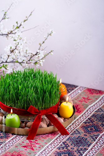 Beautiful Novruz tray on rug with semeni - wheat grass with red ribbon, festive candles on national Azerbaijani carpet table cloth with blooming branch,Spring equinox and new year celebration in Baku.