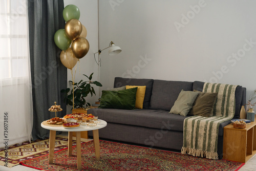 Corner of cozy living room with comfortable couch with cushions standing next to small table with snacks prepared for celebrating Eid al-Fitr photo