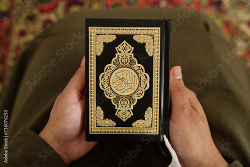Top view of hands of young unrecognizable Muslim woman holding Holy Quran with frame and ornaments on its cover before reading it photo