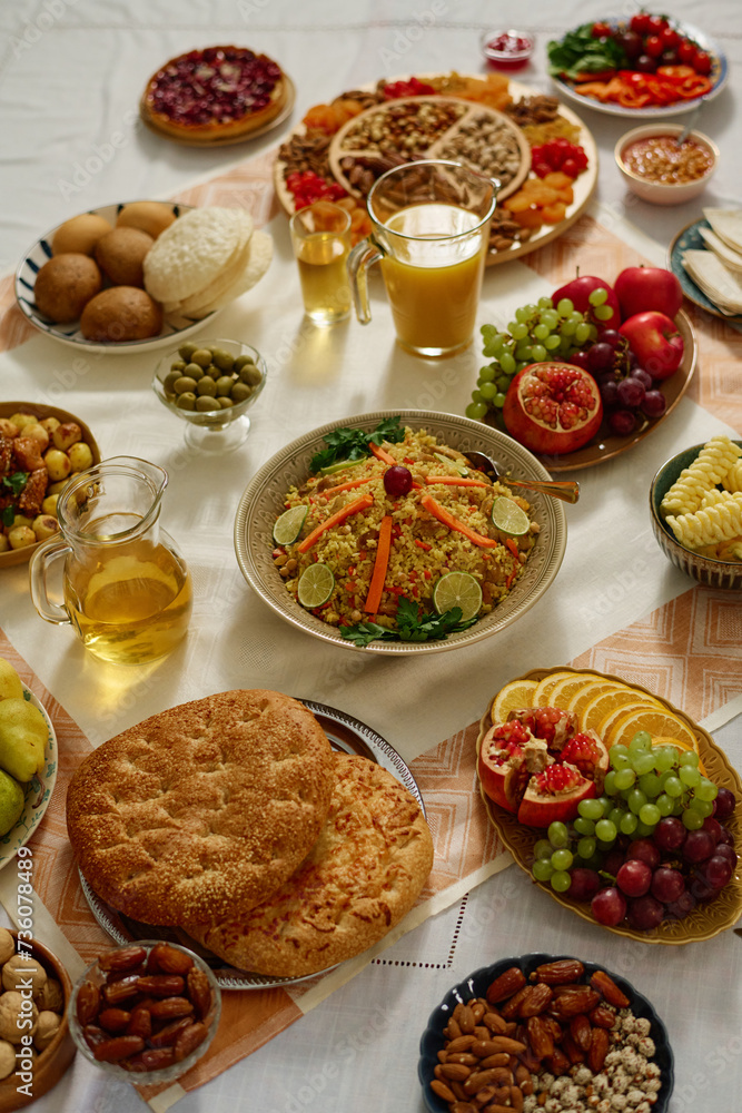 Plates with appetizing homemade pilaf and flatbread standing among fresh and dried fruits, nuts, juice and other food on tablecloth Plates with appetizing homemade pilaf and flatbread standing among fresh and dried fruits, nuts, juice and other food on tablecloth