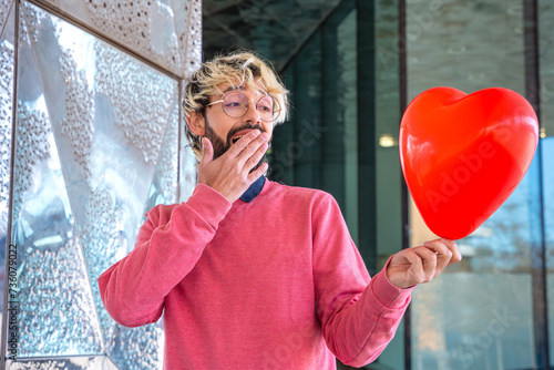 Surprised young man standing holding a heart shaped balloon. Love photo