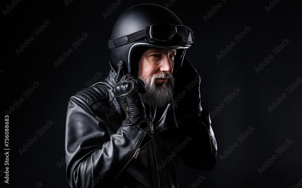 Portrait d'un motard homme avec un casque noir et une veste en cuir et des lunettes de protection et une barbe grise vintage Portrait d'un motard homme avec un casque noir et une veste en cuir et des lunettes de protection et une barbe grise vintage