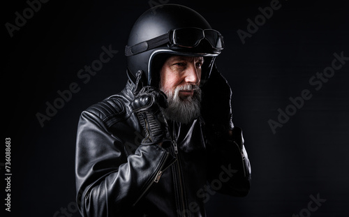 Portrait d'un motard homme avec un casque noir et une veste en cuir et des lunettes de protection et une barbe grise vintage photo
