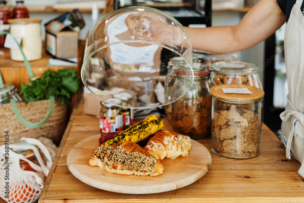 © nataliaderiabina - Seller in apron showing freshly croissants and healthy vegan bakery products in zero waste shop. © nataliaderiabina - Seller in apron showing freshly croissants and healthy vegan bakery products in zero waste shop.