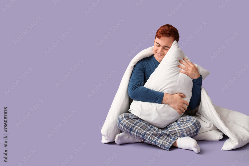 Handsome young happy man with blanket and pillow sitting on purple background Handsome young happy man with blanket and pillow sitting on purple background