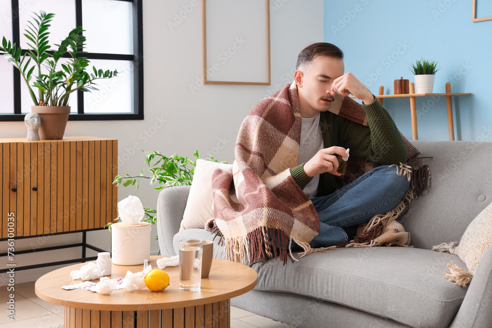 Ill young man with plaid and nasal drops sitting on sofa at home Ill young man with plaid and nasal drops sitting on sofa at home