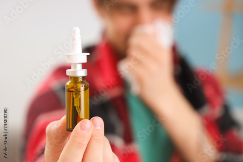 Sick young man with nasal drops at home, closeup