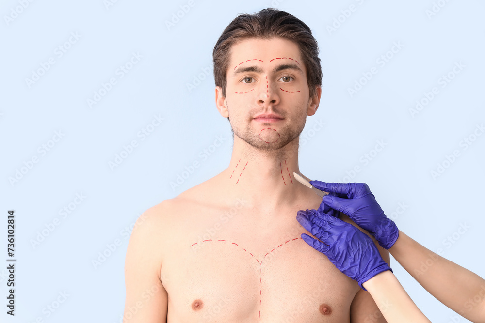 Plastic surgeon with scalpel and markings on young man's body against blue background, closeup