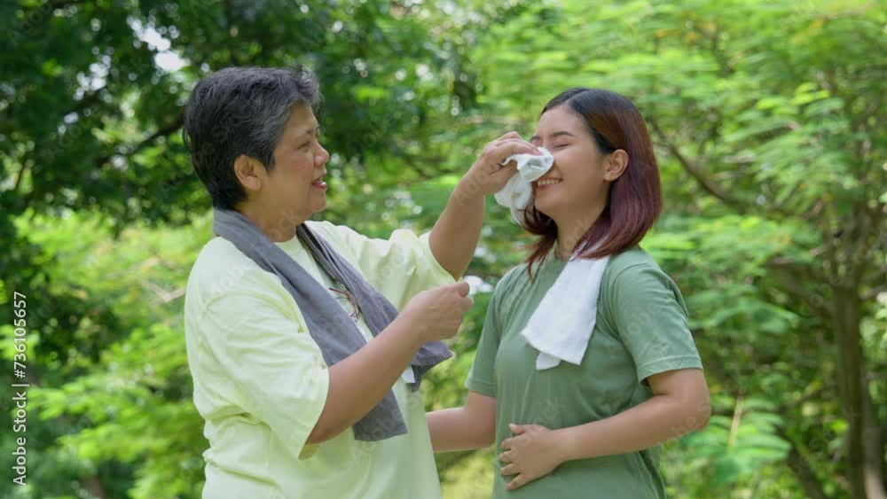 Attractive Senior mother and daughter working out together in the morning exercise in the park. Daughter absorbs sweat from her mom with white towel, a senior caregiver, and a happy family concept. Attractive Senior mother and daughter working out together in the morning exercise in the park. Daughter absorbs sweat from her mom with white towel, a senior caregiver, and a happy family concept.