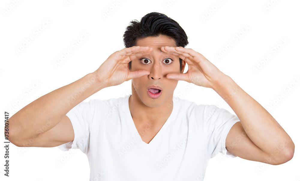 Naklejka premium Closeup portrait of young, curious funny man, student, employee looking through his fingers like binoculars, surprised, shocked by what he found in future, isolated on white background