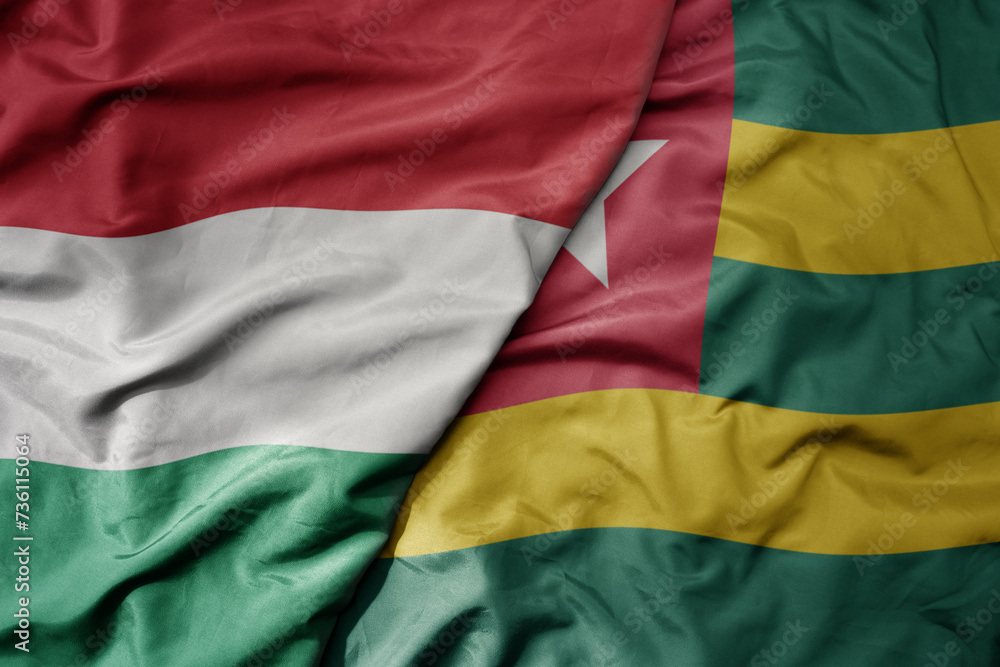 big waving national colorful flag of togo and national flag of hungary .