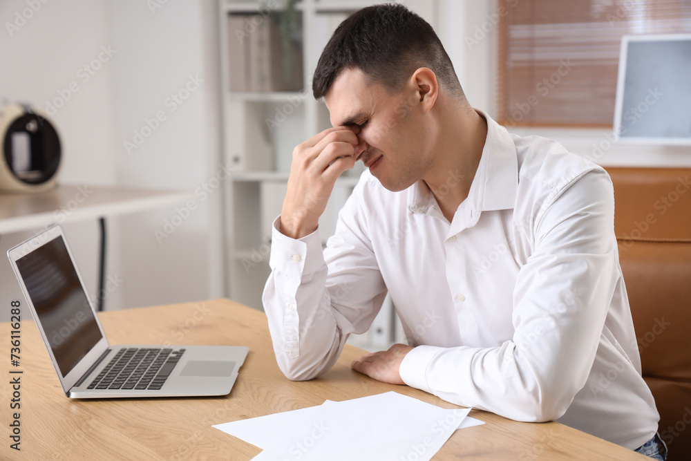 Young businessman suffering from headache in office Young businessman suffering from headache in office