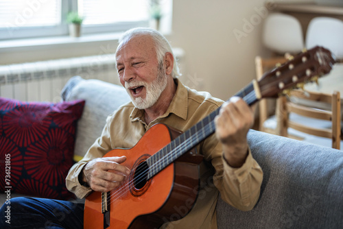A lonely man with a beard enjoys playing the guitar at home. Senior man playing guitar at home.