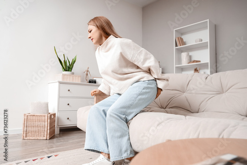 Mature woman with hemorrhoids sitting on sofa at home photo