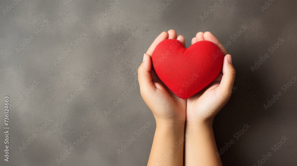 Obraz premium Child's hands holding red paper heart on neutral background