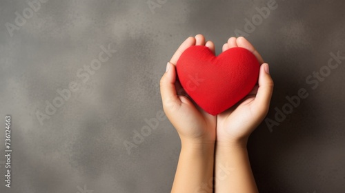 Child s hands holding red paper heart on neutral background