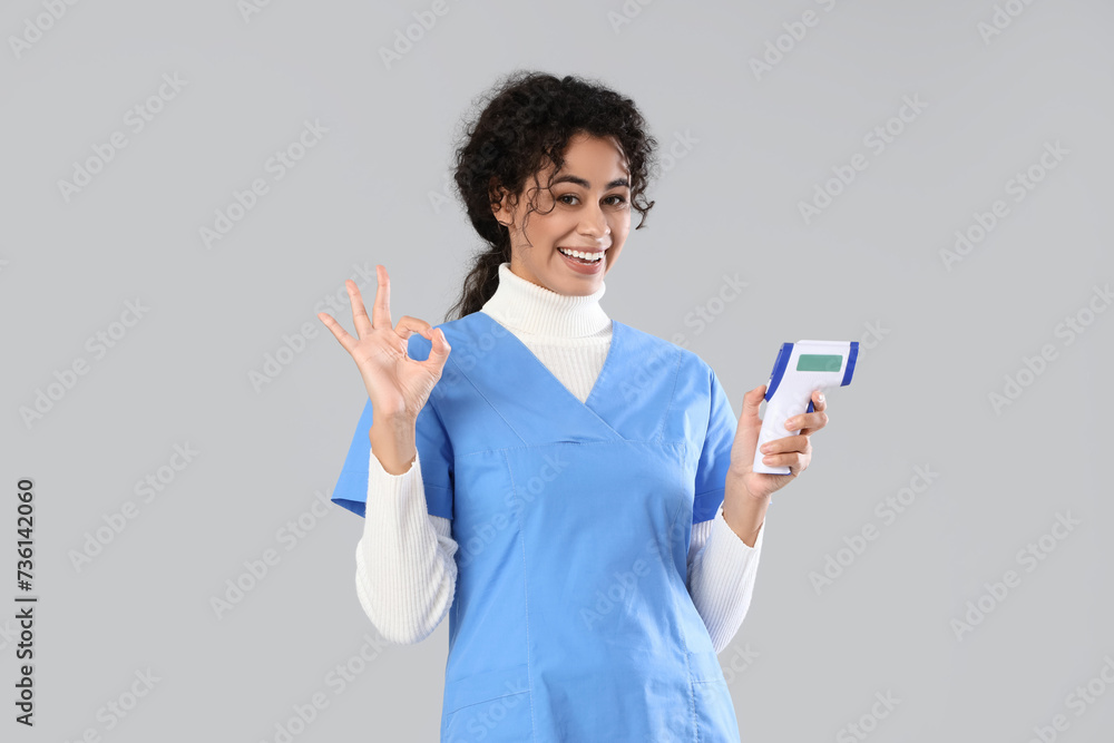 Female African-American medical intern with infrared thermometer showing OK on light background Female African-American medical intern with infrared thermometer showing OK on light background