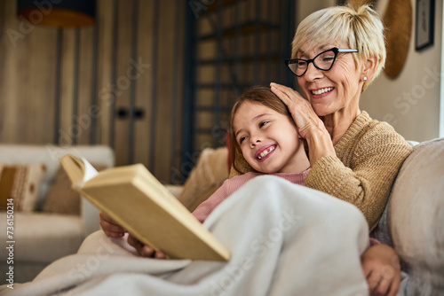 Grandma and grandchild spending time together, covered in a blanket, reading a book together.