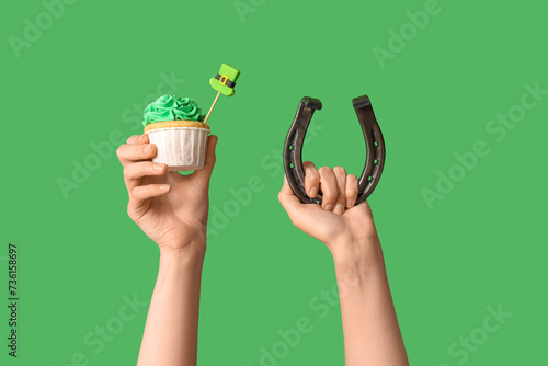 Female hands with tasty cupcake and horseshoe for St. Patrick's Day on green background