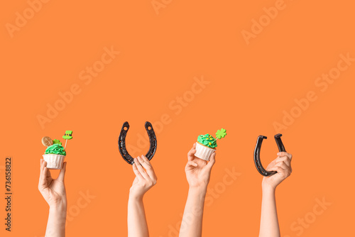 Female hands with tasty cupcakes and horseshoes for St. Patrick's Day on orange background photo