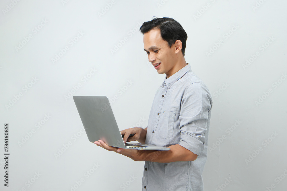 happy asian indonesian man holding laptop computer on isolated background happy asian indonesian man holding laptop computer on isolated background