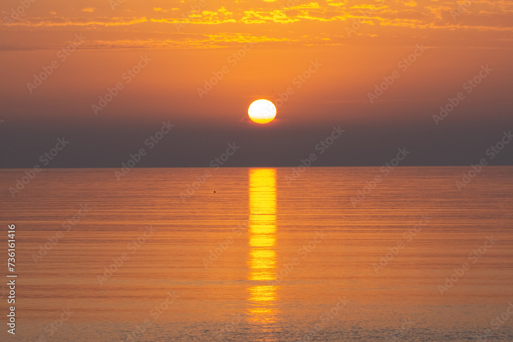 The sun rising over the horizon forms a golden glow over the sea at sunrise on Paignton Beach in Devon