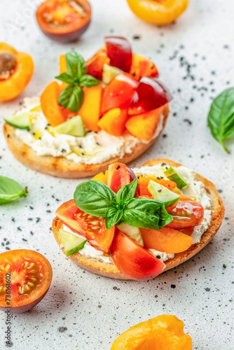 Open sandwiches with cream cheese, peaches, tomatoes and green basil leaves on white background. top view