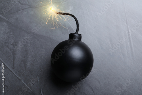 Old fashioned black bomb with lit fuse on grey table, top view