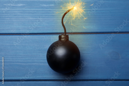 Old fashioned black bomb with lit fuse on blue wooden table, top view photo