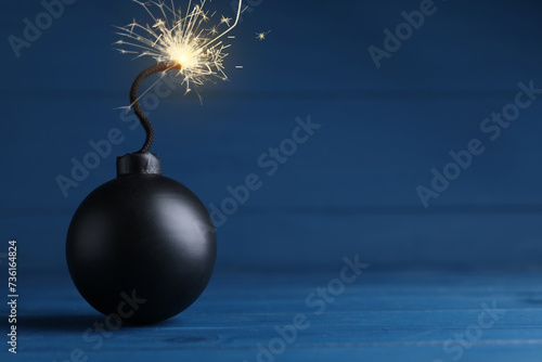Obraz na plátně Old fashioned black bomb with lit fuse on blue wooden table, space for text
