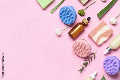 Hair scalp massagers with shampoo bars, bottles of cosmetic products and flowers on pink background photo