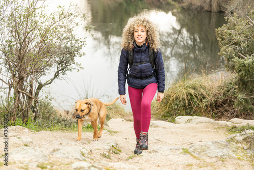 Curly and blonde hair, mountaineer woman and her dog walking through the mountains.