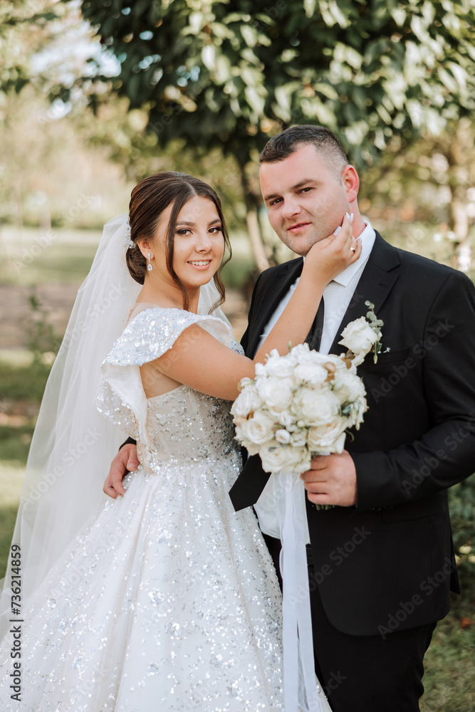 Stylish, young groom and beautiful bride in a long white dress and a long veil with a bouquet in their hands, hugging in the park in the autumn nature. Wedding portrait of newlyweds. Stylish, young groom and beautiful bride in a long white dress and a long veil with a bouquet in their hands, hugging in the park in the autumn nature. Wedding portrait of newlyweds.