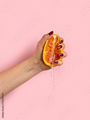 Female hand with half of juicy orange  on pink background. Sex concept.